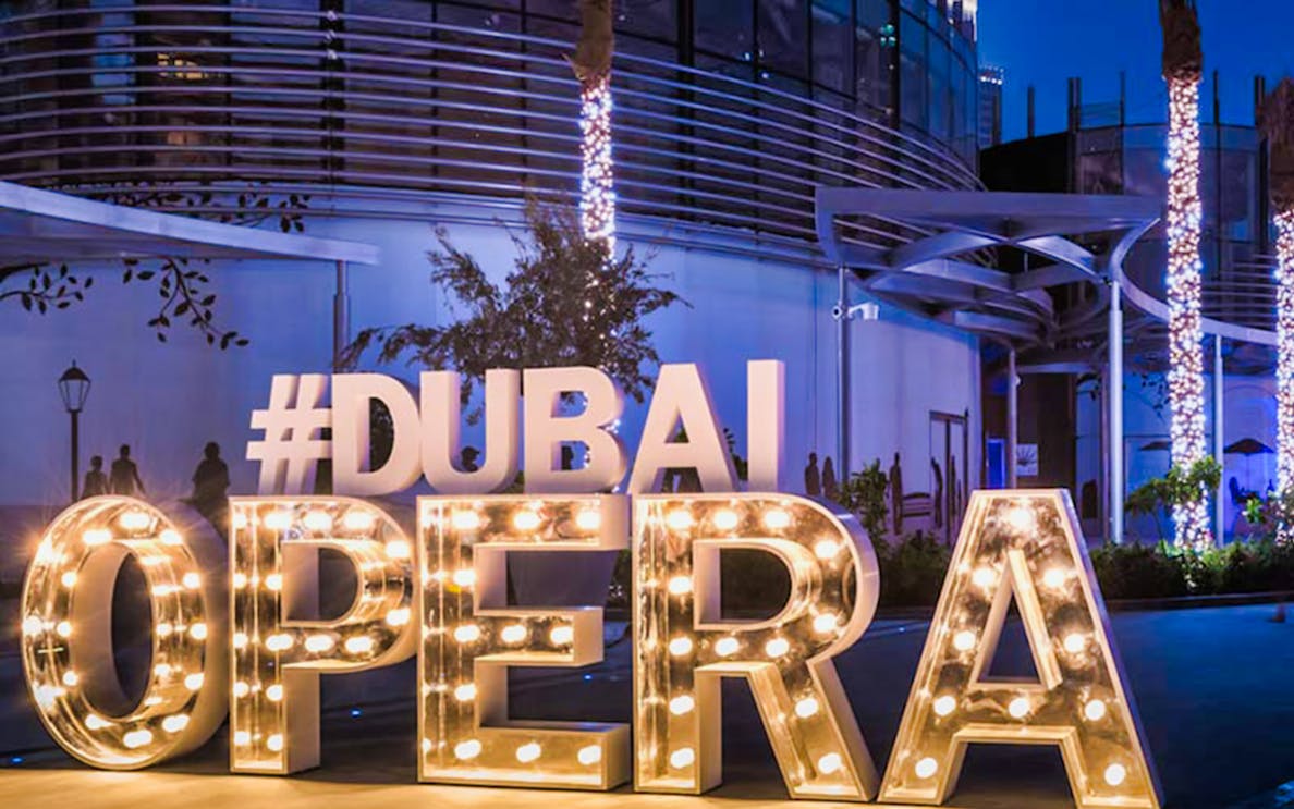 Dubai Opera entrance lit up at night, promoting the Mamma Mia show.