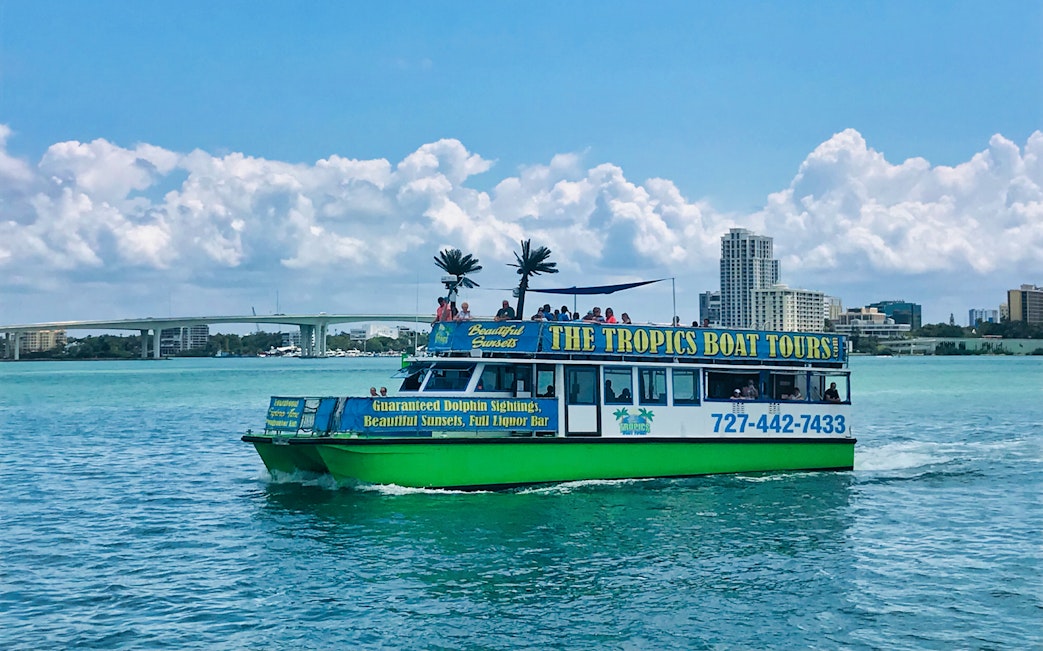 Tour boat cruising in the Gulf of Mexico with city skyline and bridge in the background.