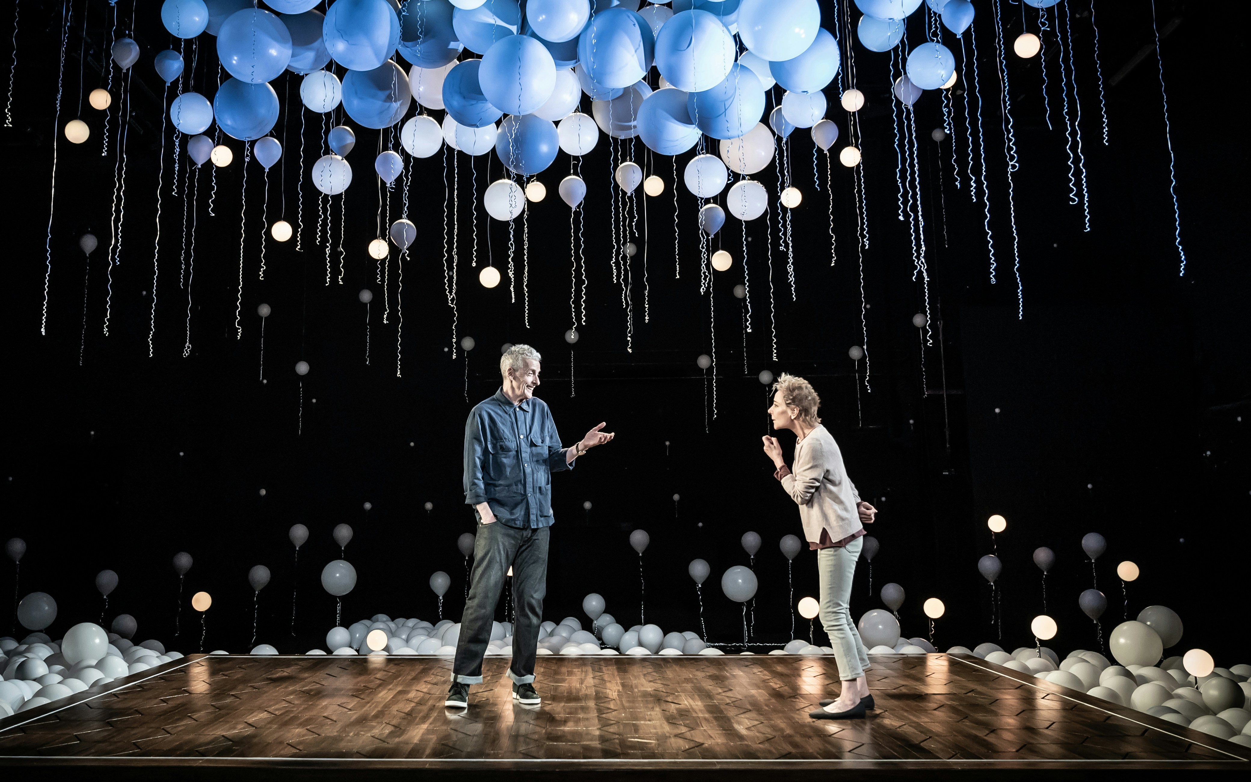 Two people on stage under hanging blue and white balloons, part of "Constellations" play.