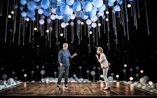 Two people on stage under hanging blue and white balloons, part of "Constellations" play.