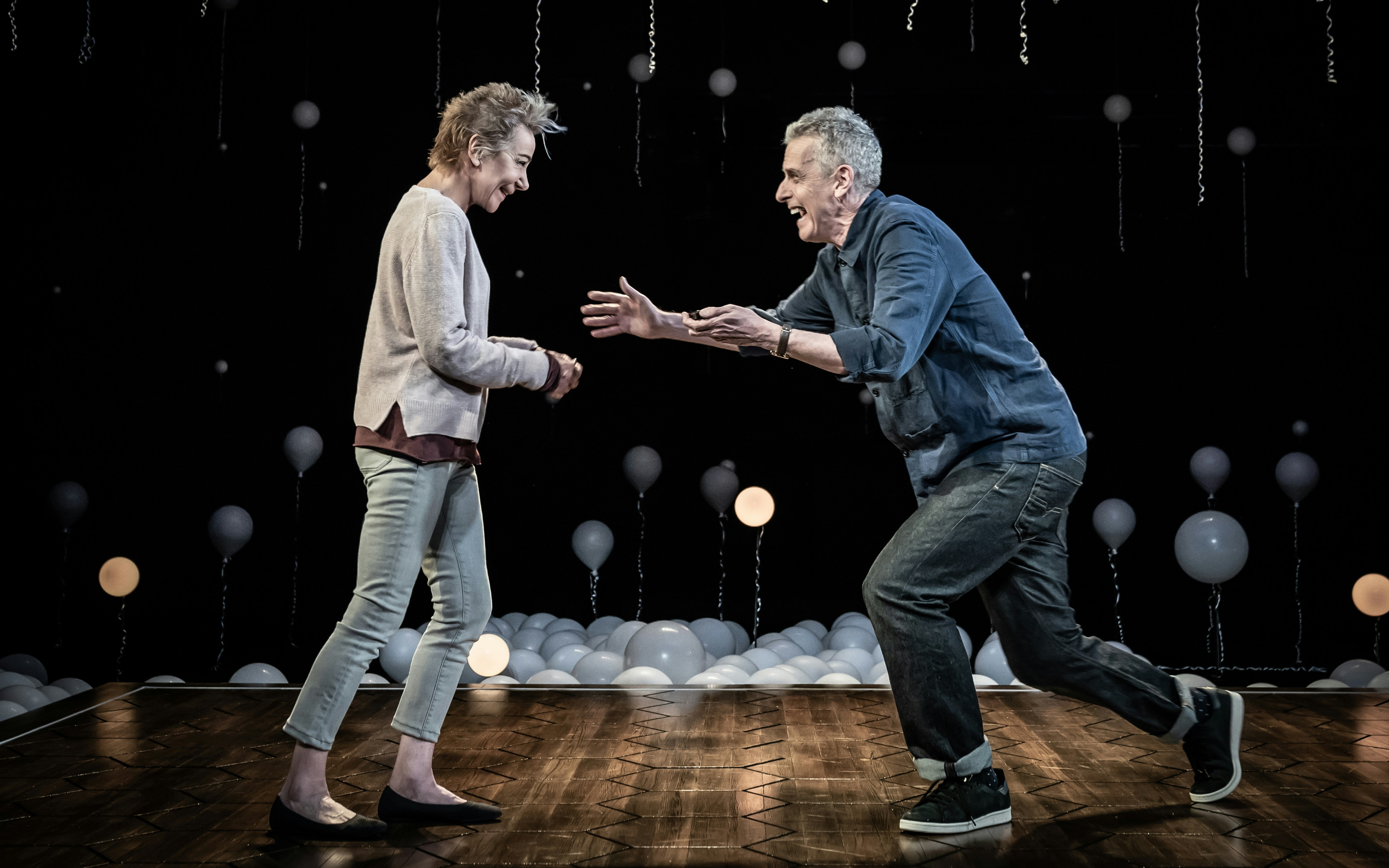 Two people interacting on stage with balloons in the background, related to "Constellations" play.