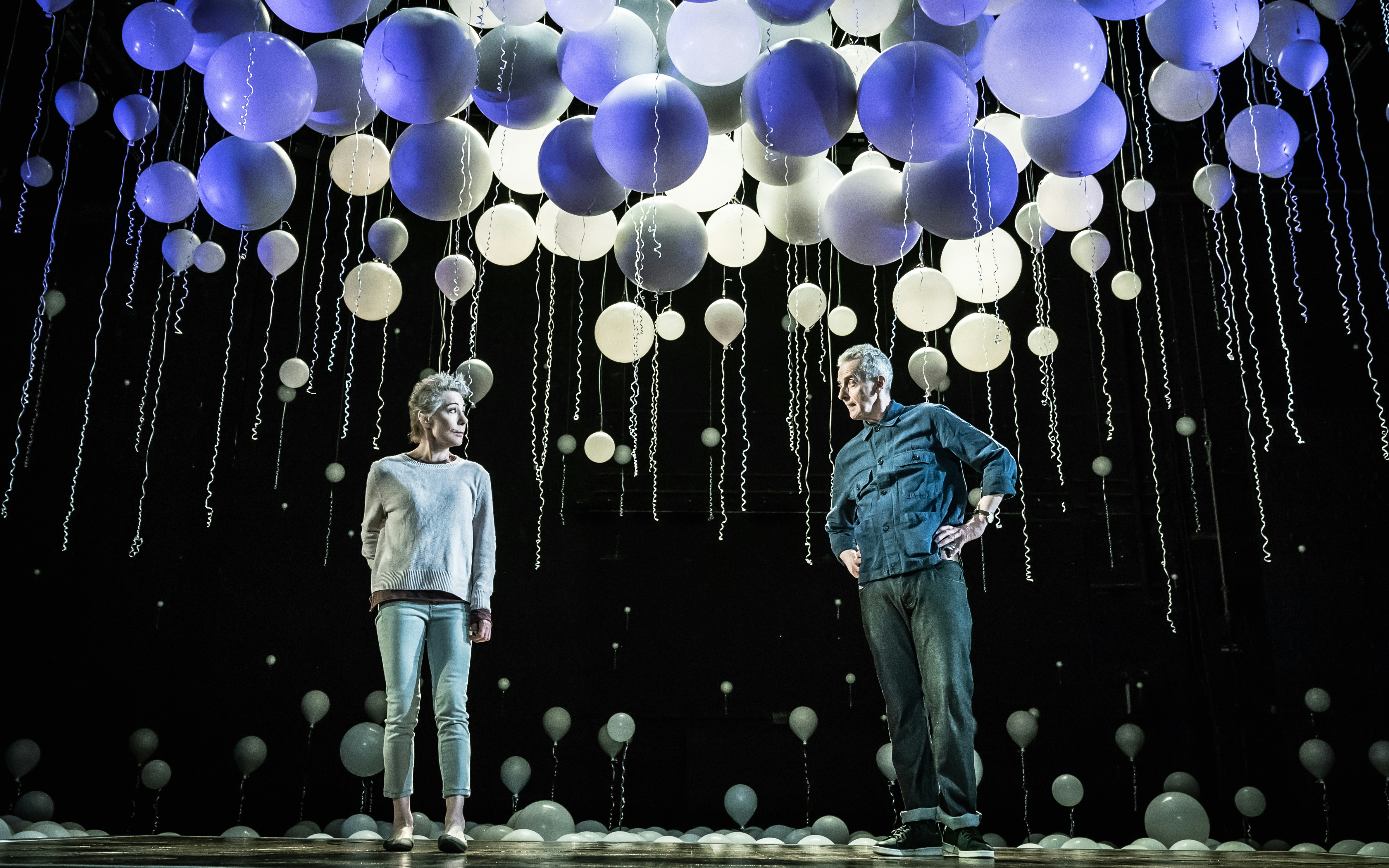 Two people stand on stage under a ceiling of hanging balloons, resembling constellations.