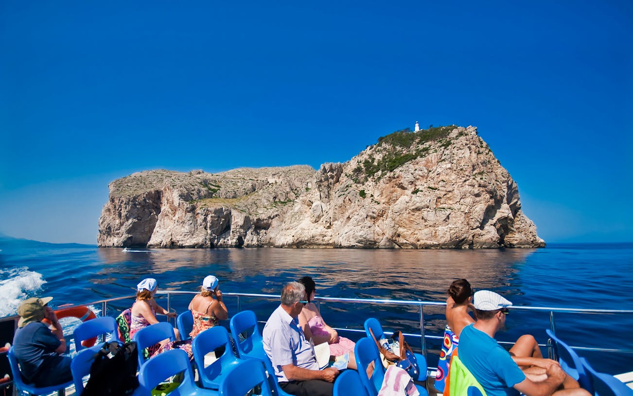 Tourists on a boat viewing rocky coastline during Palma Mallorca walking tour.