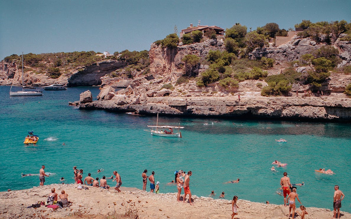 People enjoying a kayak excursion and swimming in the clear waters of Mallorca with rocky cliffs in the background.