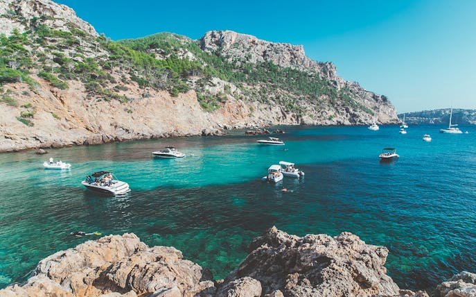 Boats in a turquoise bay with rocky cliffs in Majorca, Spain.