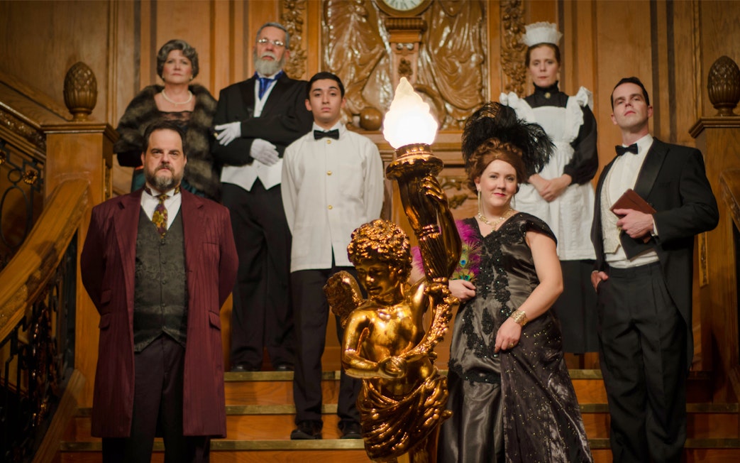 Group in period costumes on Titanic's grand staircase at artifact exhibition.