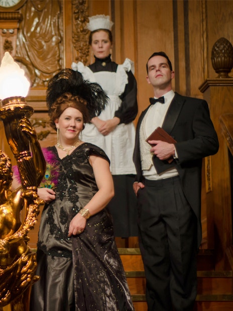 Group in period costumes on Titanic's grand staircase at artifact exhibition.