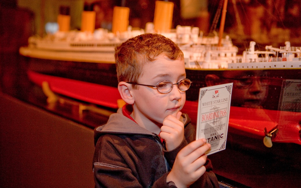 Child examining Titanic boarding pass at artifact exhibition.