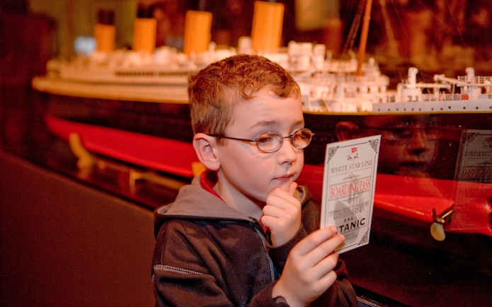 Child examining Titanic boarding pass at artifact exhibition.