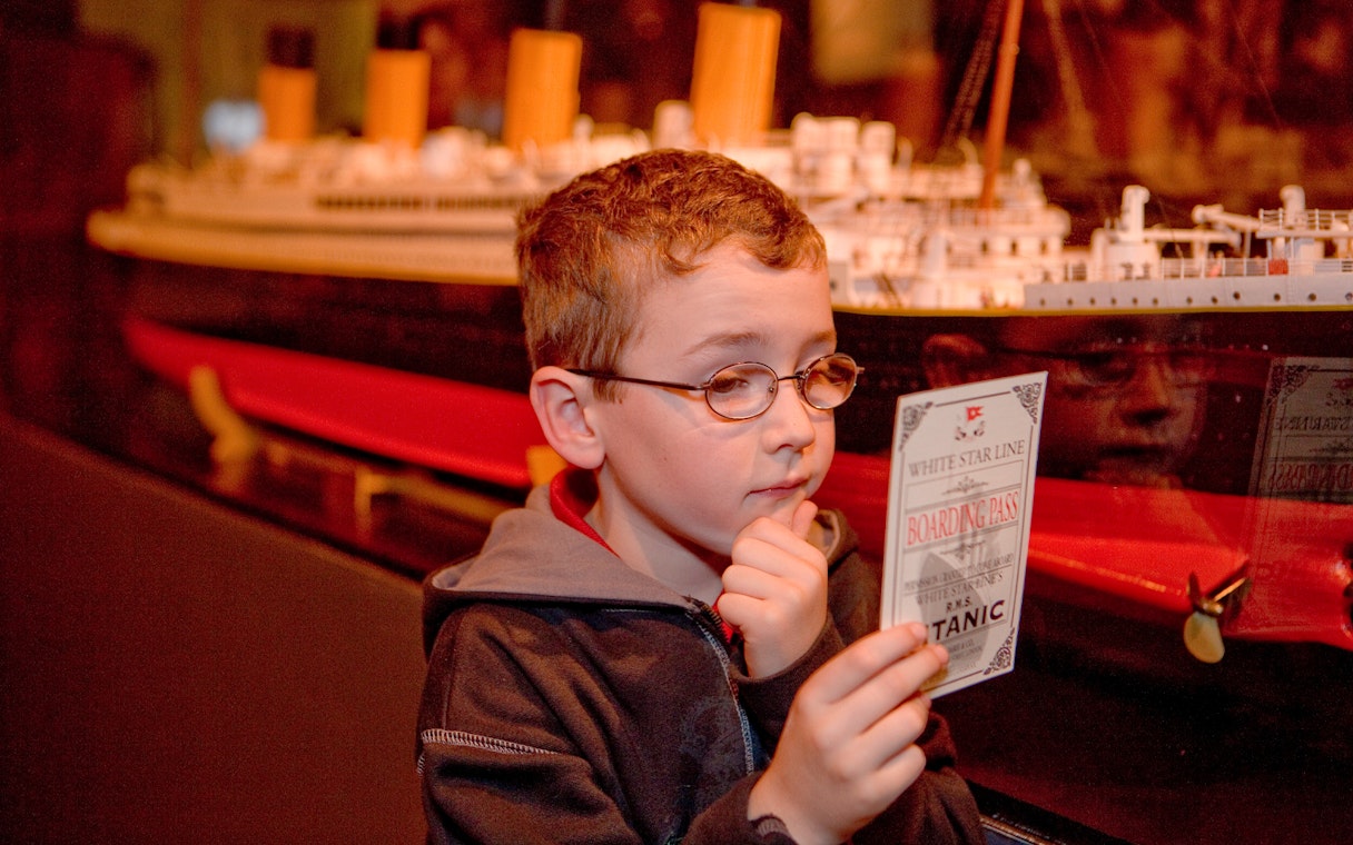 Child examining Titanic boarding pass at artifact exhibition.