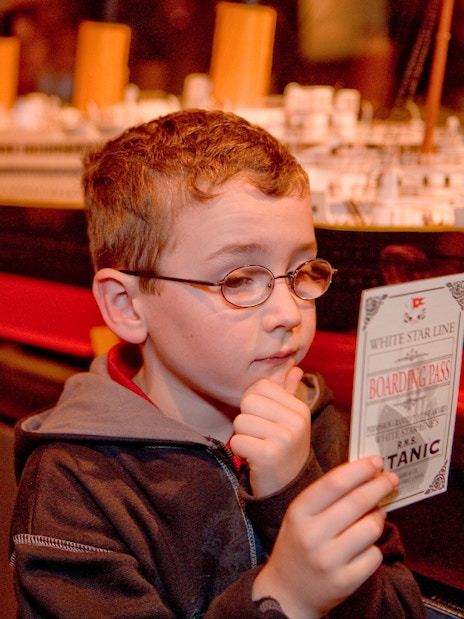 Child examining Titanic boarding pass at artifact exhibition.