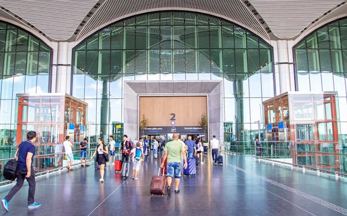 Travelers with luggage at Sabiha Gokcen Airport entrance, Istanbul.