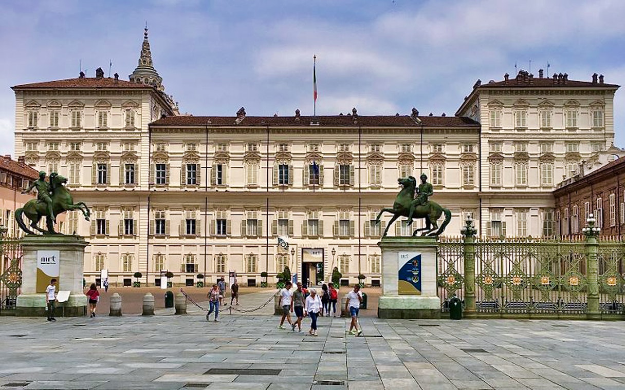 Royal Palace of Turin facade with equestrian statues and visitors in the foreground.