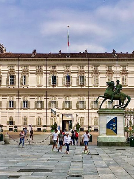 Royal Palace of Turin facade with equestrian statues and visitors in the foreground.