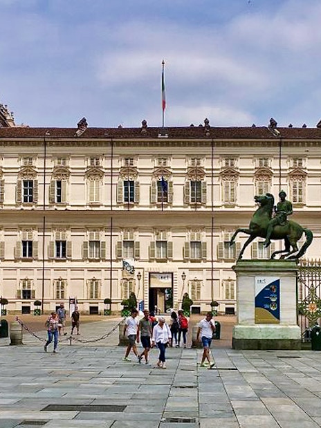 Royal Palace of Turin facade with equestrian statues and visitors in the foreground.