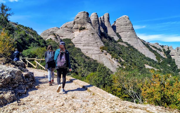 Hikers on a trail with Montserrat mountain peaks in the background, Spain.