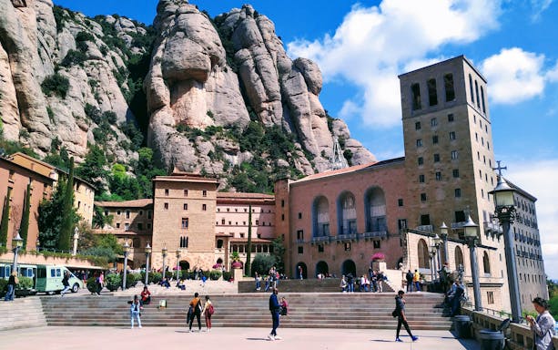 Montserrat Monastery with visitors, nestled against rocky cliffs, Spain.