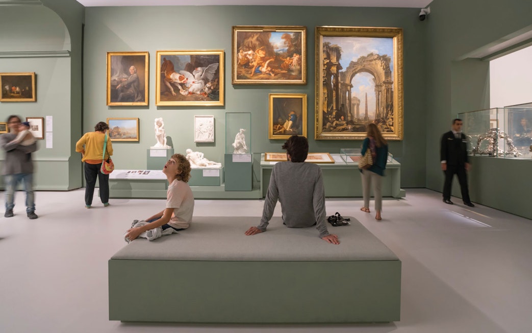 Visitors observing art and sculptures in a gallery at Louvre Museum Abu Dhabi.
