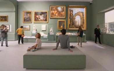 Visitors observing art and sculptures in a gallery at Louvre Museum Abu Dhabi.