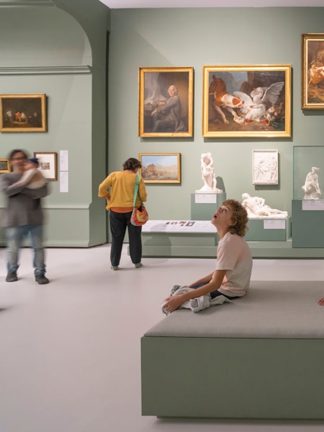 Visitors observing art and sculptures in a gallery at Louvre Museum Abu Dhabi.