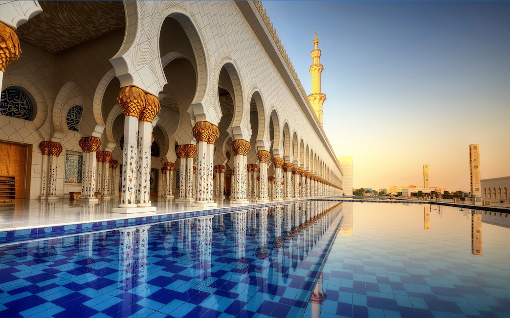 Abu Dhabi Mosque exterior with reflection in water, part of guided tour including Louvre Museum.