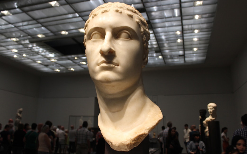 Bust of a Roman figure displayed at Louvre Museum Abu Dhabi with visitors in the background.