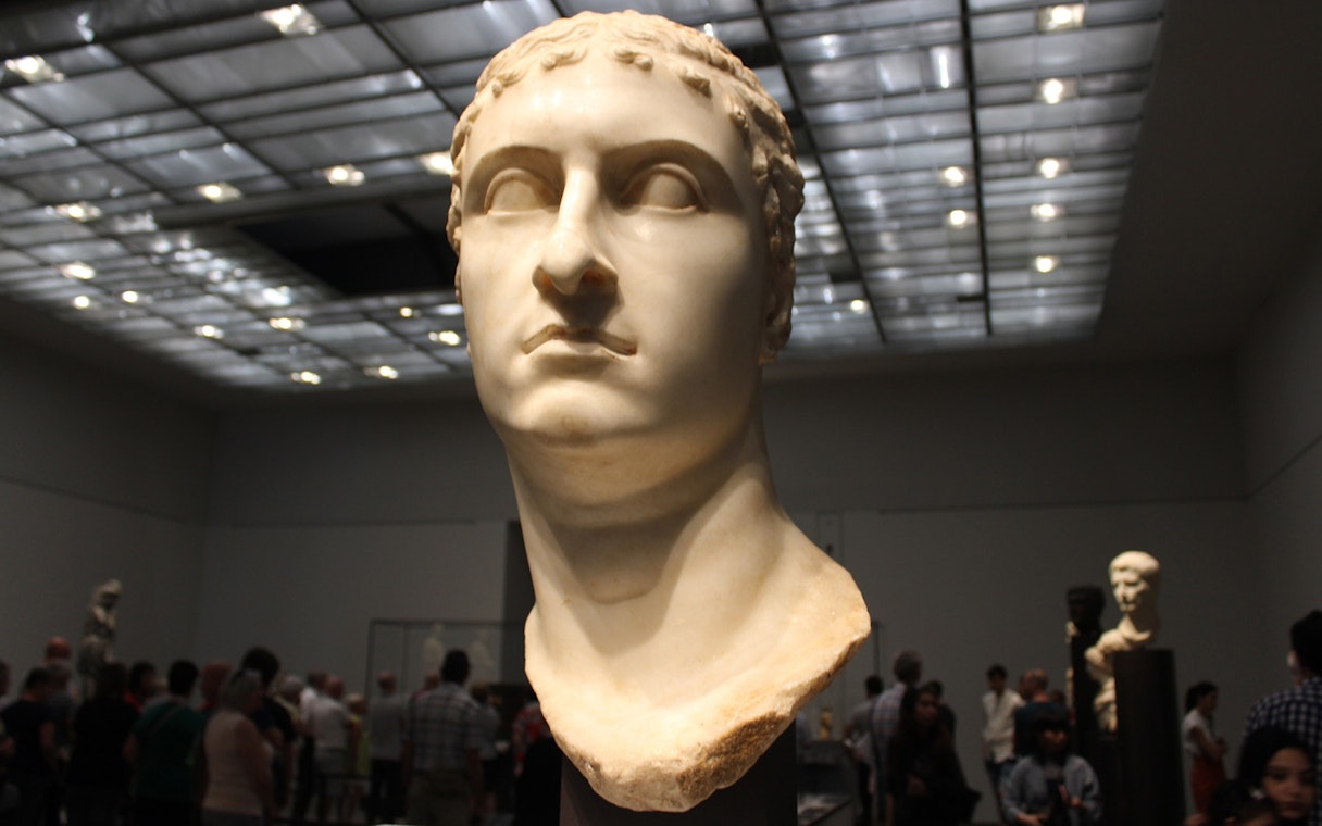 Bust of a Roman figure displayed at Louvre Museum Abu Dhabi with visitors in the background.