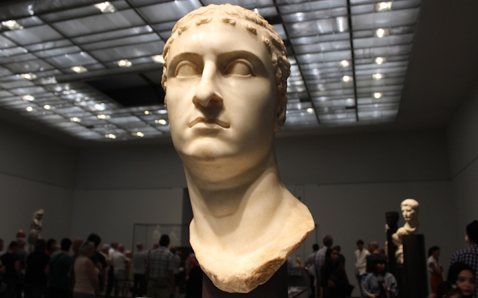 Bust of a Roman figure displayed at Louvre Museum Abu Dhabi with visitors in the background.