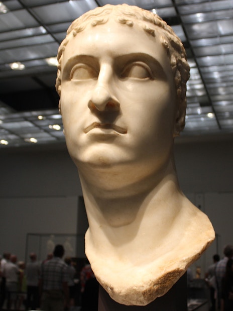 Bust of a Roman figure displayed at Louvre Museum Abu Dhabi with visitors in the background.