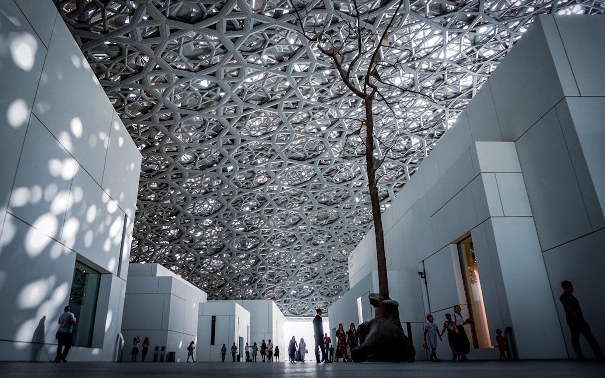 Louvre Abu Dhabi interior with geometric ceiling and visitors walking.