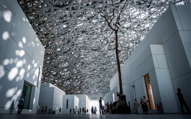 Louvre Abu Dhabi interior with geometric ceiling and visitors walking.