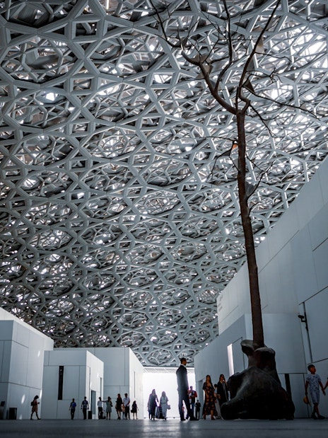 Louvre Abu Dhabi interior with geometric ceiling and visitors walking.