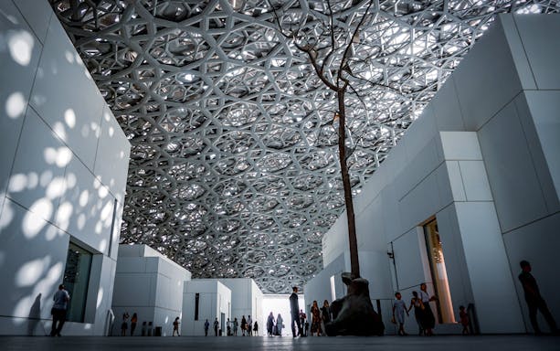 Louvre Abu Dhabi interior with geometric ceiling and visitors walking.