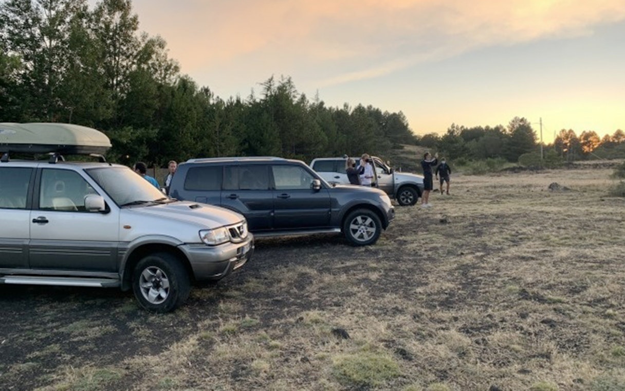 Jeep tour group at Mount Etna with sunset and forest backdrop.