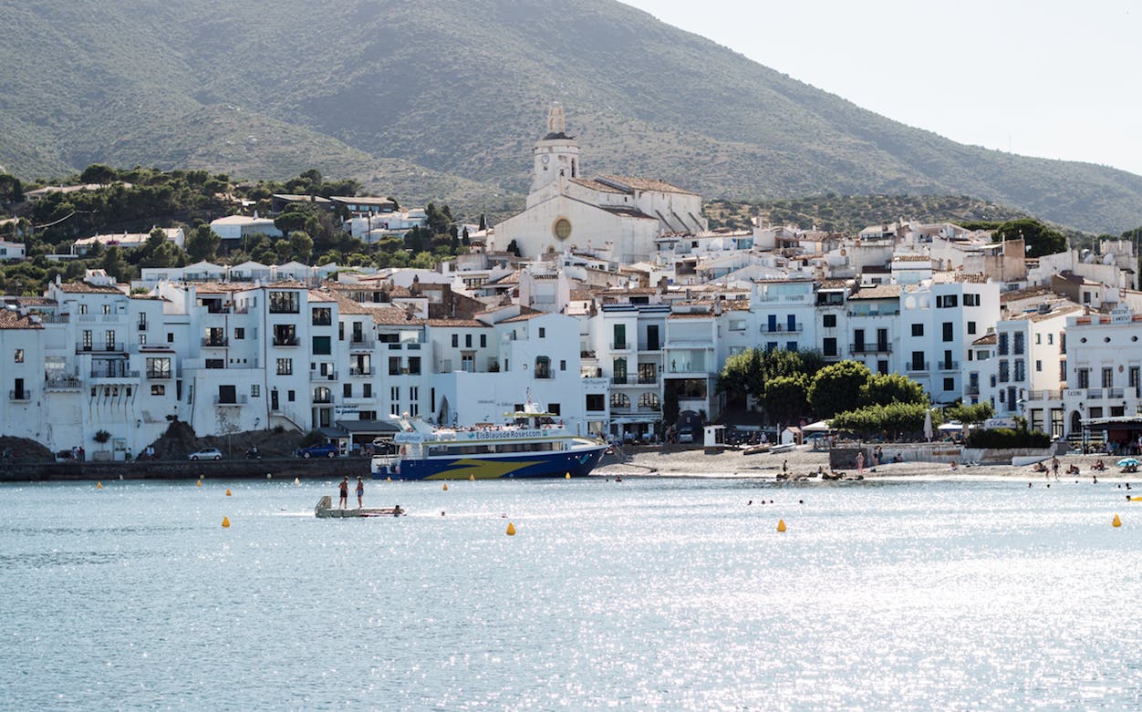 Cadaqués waterfront with white buildings and a boat in the bay, Spain.