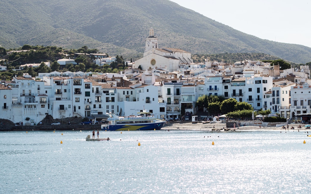 Boat approaching Cadaqués with white buildings and church in the background.