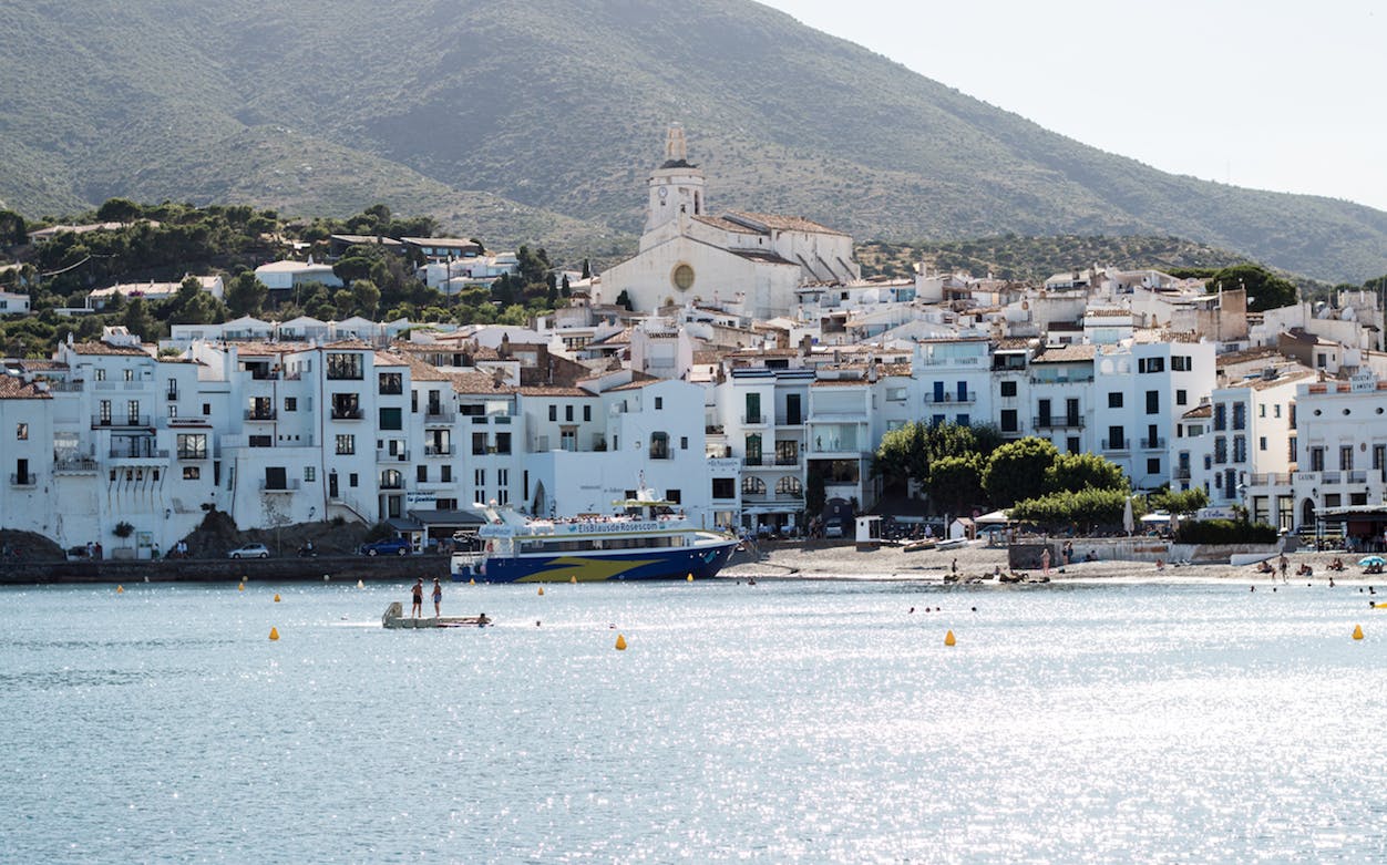 Boat approaching Cadaqués with white buildings and church in the background.