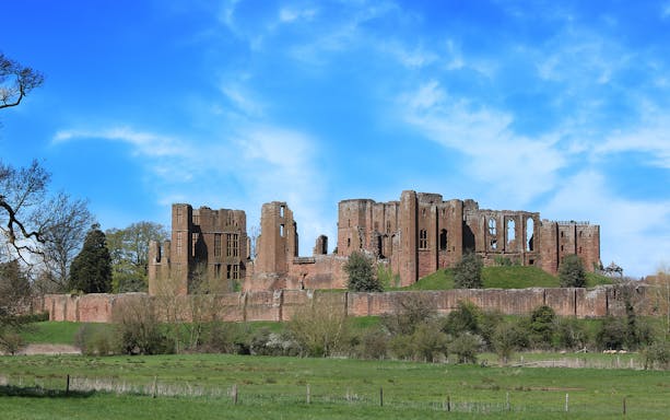 Kenilworth Castle ruins with surrounding greenery under a blue sky in Warwickshire, England.