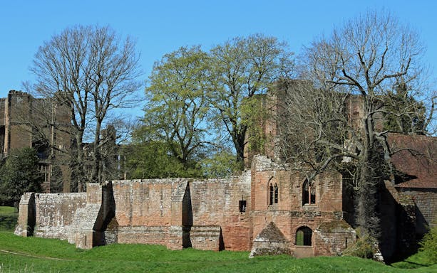 Kenilworth Castle ruins with surrounding trees under a clear blue sky.