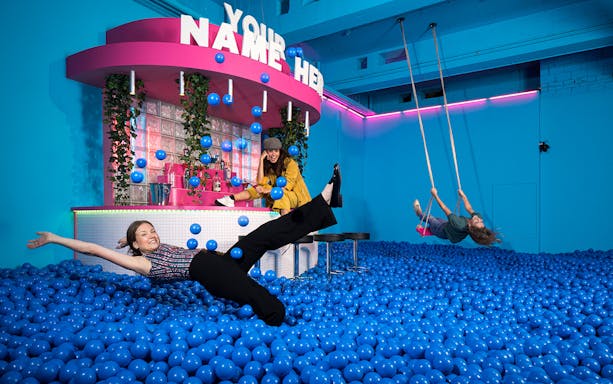 Visitors enjoying interactive exhibits at Youseum, surrounded by blue balls and swings.