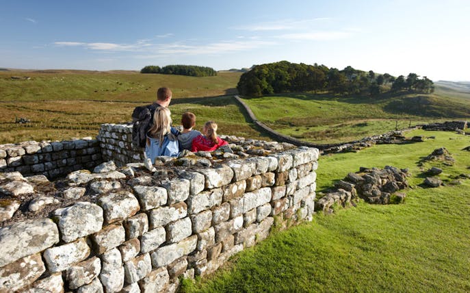 Family exploring Housesteads Roman Fort with scenic countryside view.