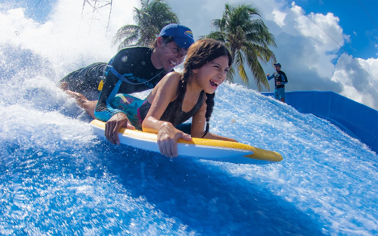 Child and instructor surfing on FlowRider wave simulator in Cancun.