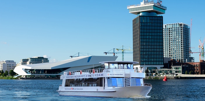 Tour boat cruising in front of A'DAM Tower and EYE Film Museum, Amsterdam Harbor.