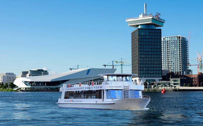 Tour boat cruising in front of A'DAM Tower and EYE Film Museum, Amsterdam Harbor.