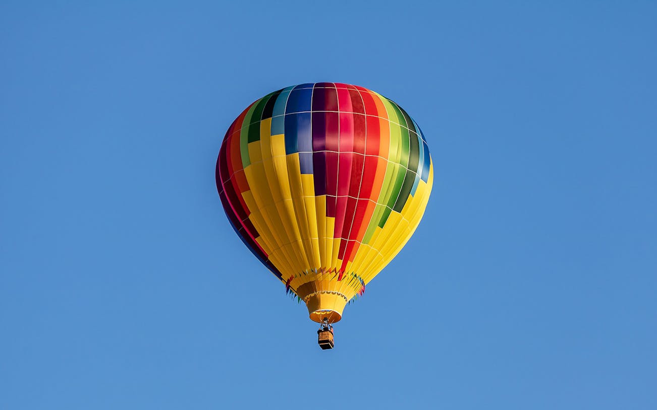 Colorful hot-air balloon floating in clear blue sky, Prague tour.