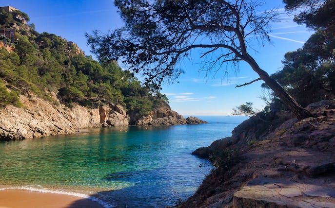 Coastal hiking trail view in Tossa de Mar, Costa Brava, with rocky cliffs and clear blue water.