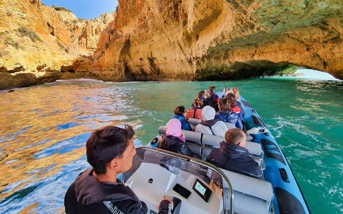 Boat tour entering Benagil Cave with tourists, Algarve coast, Portugal.