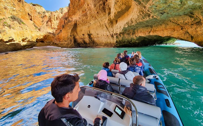 Boat tour entering Benagil Cave with tourists, Algarve coast, Portugal.