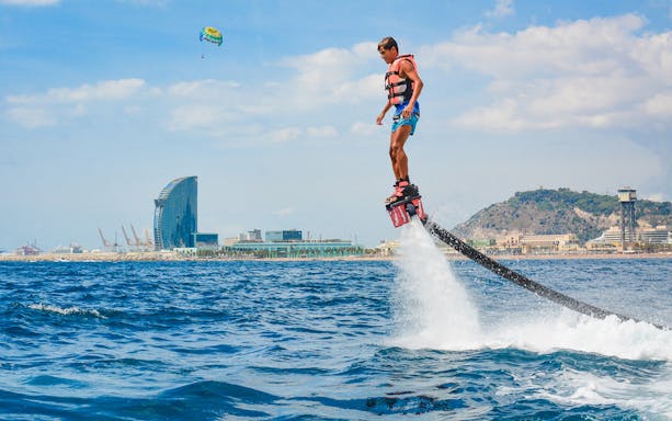 Person flyboarding over the sea with Barcelona skyline in the background.