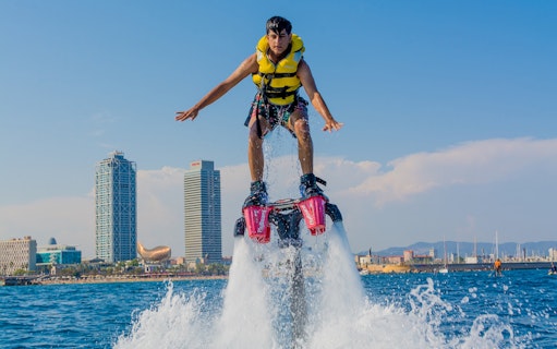 Flyboarder soaring over water with Barcelona skyline in background.